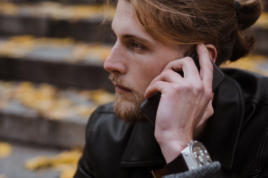 Close-up of a young man with a beard talking on his phone outdoors in autumn.