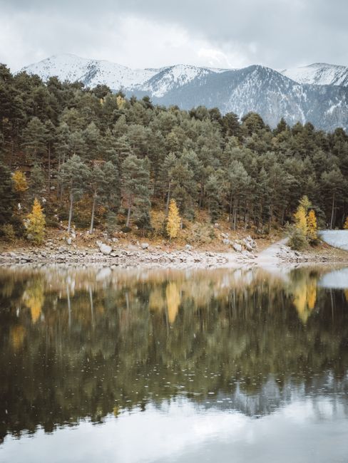 Peaceful lake in Engolasters, Andorra, reflecting dense forests and snow-capped peaks.