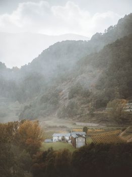A foggy landscape with houses in a valley surrounded by mountains and trees in Ordino, Andorra.