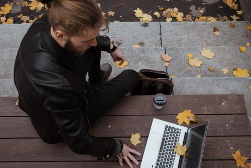 Free Bearded man with a laptop on a wooden bench, surrounded by autumn leaves. Stock Photo