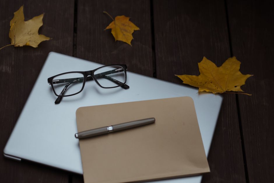 AI Writing Prompts That Actually Produce Quality Content A cozy autumn workspace featuring a laptop, eyeglasses, and leaves on a wooden table.
