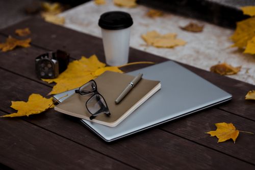 Free Outdoor autumn workspace setup with laptop, notebook, pen, and coffee on a wooden table with fallen leaves. Stock Photo