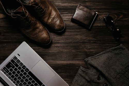 Free Modern workspace featuring laptop, leather shoes, wallet, and sunglasses on a wooden desk. Stock Photo