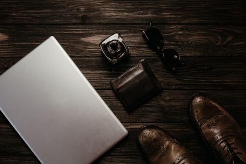 Free Flat lay of stylish essentials: leather shoes, sunglasses, and a laptop on a wooden surface. Stock Photo