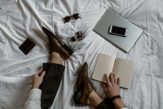Top view of a freelance workspace on a bed with a laptop, phone, notebook, and stylish accessories.