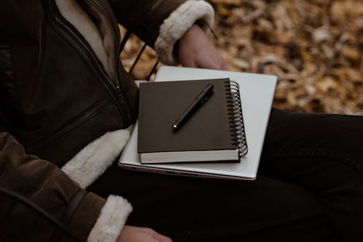 A person sitting outdoors with a notebook and laptop, surrounded by autumn leaves, representing a cozy work setup.