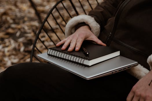 A person holds a laptop and notebook in a cozy autumn park setting, showcasing freelance essentials.