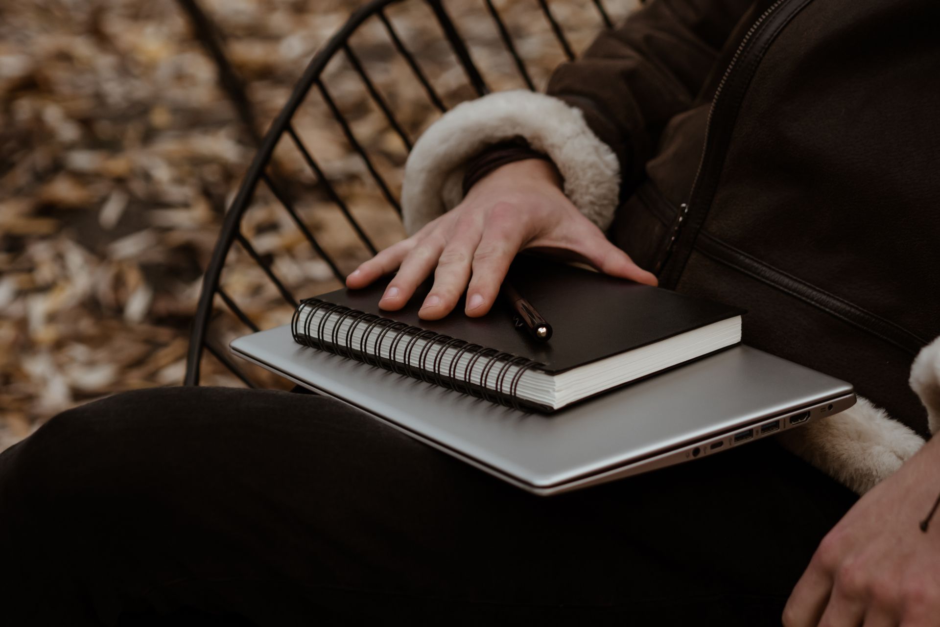 A person holds a laptop and notebook in a cozy autumn park setting, showcasing freelance essentials.