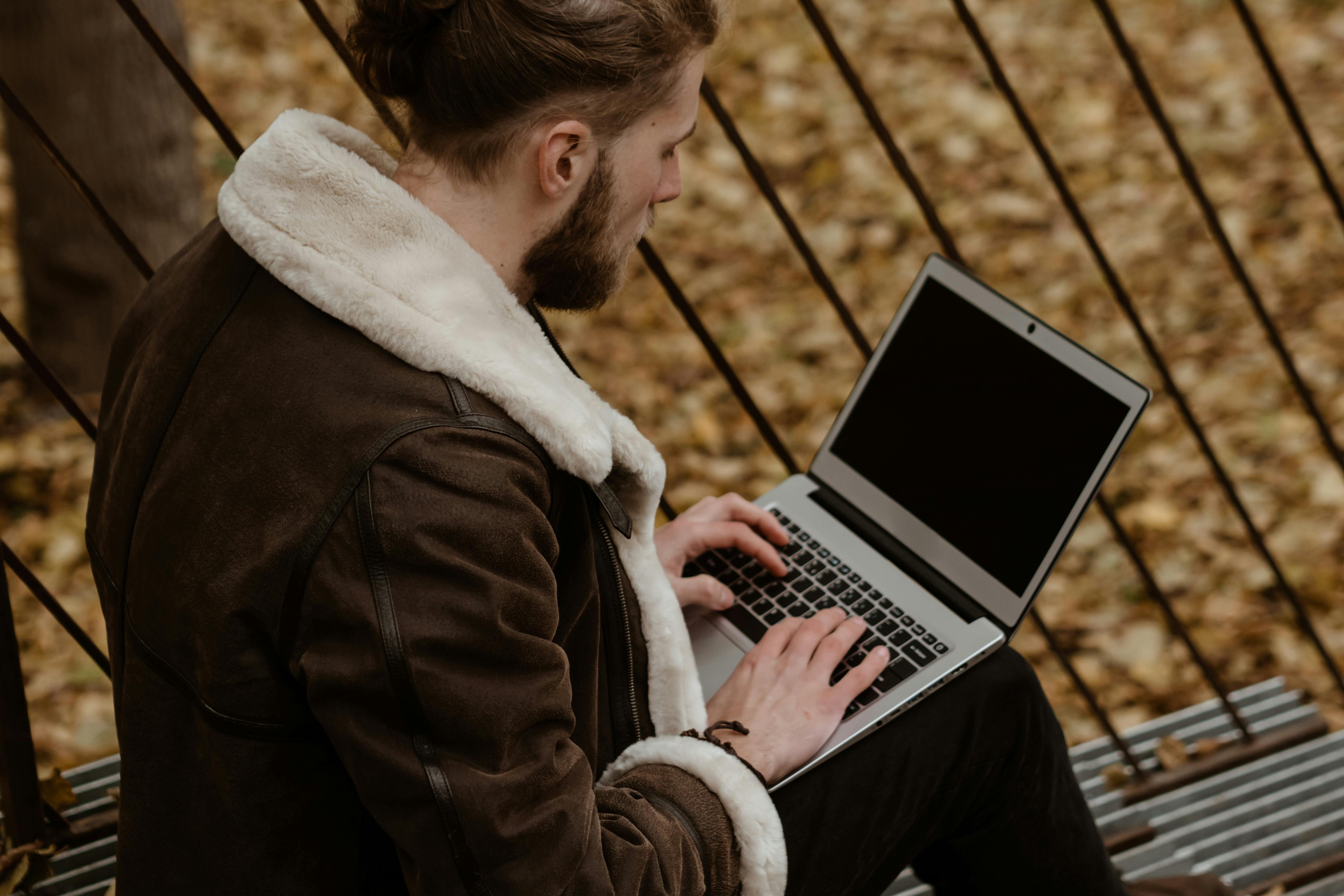 man in brown coat using macbook pro