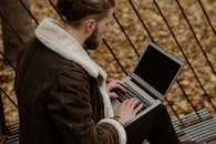 Man in Brown Coat Using Macbook Pro