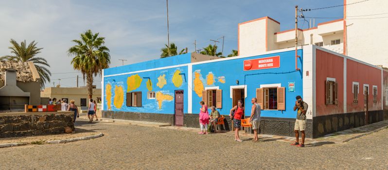 Colorful street with people and mural in a sunny tropical locale.