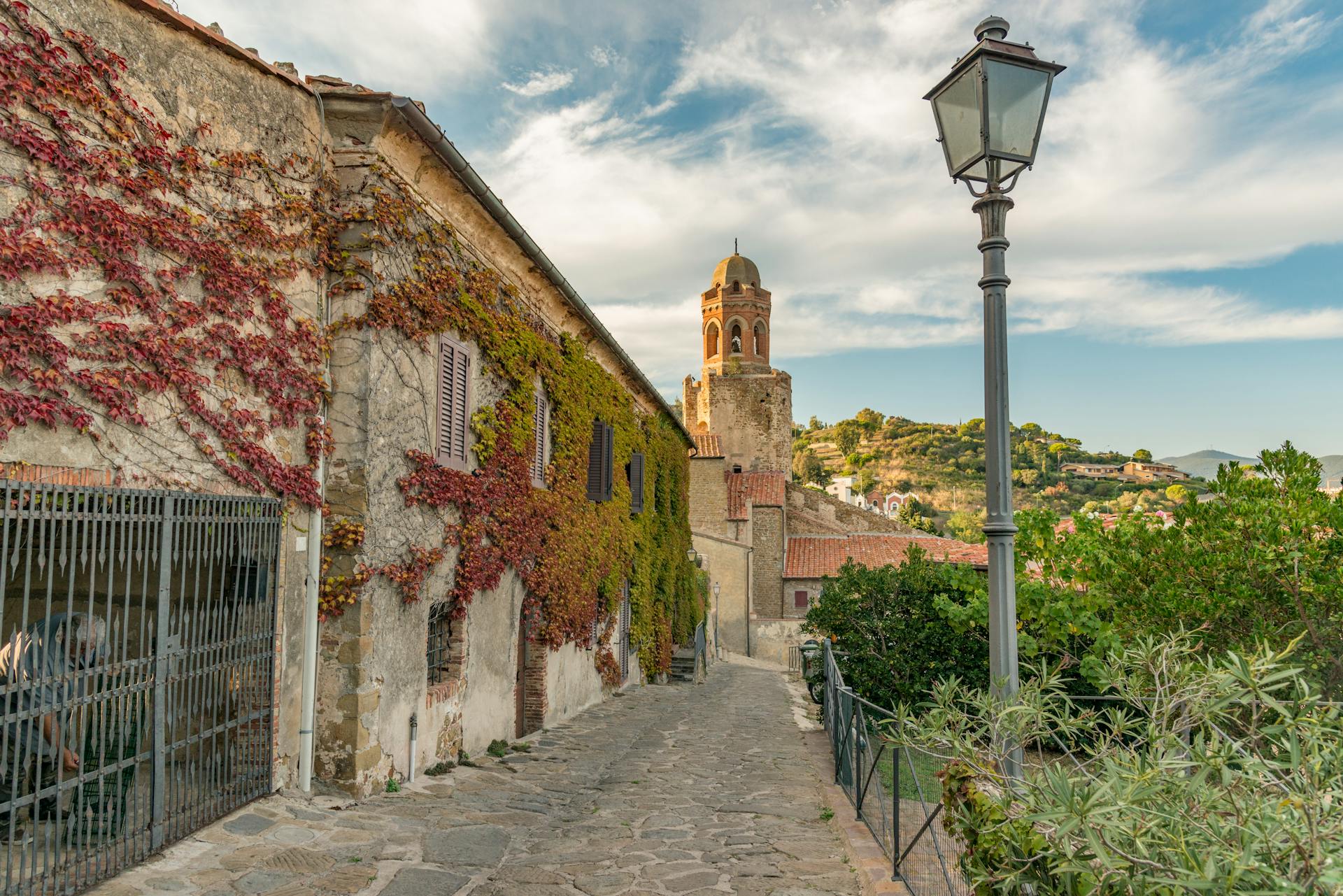 Picturesque street view in Castiglione della Pescaia, Italy, featuring ivy-clad walls and a historic church tower.