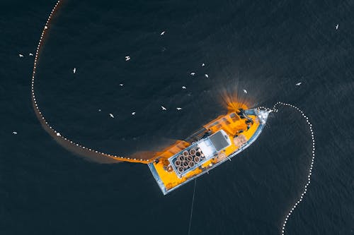 Aerial top view of modern fishing vessel with nets floating on dark seawater in daylight