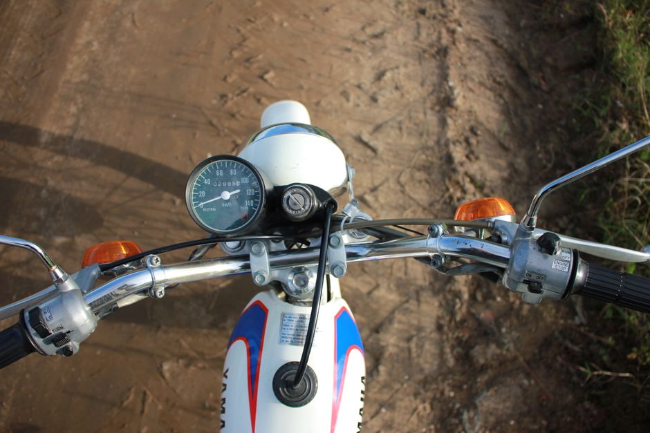View of motorcycle handlebars and gauges on unpaved road.