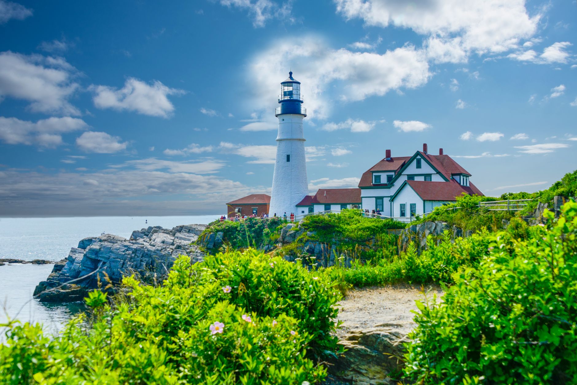 Scenic view of Portland Head Light in Maine with lush greenery and ocean backdrop.