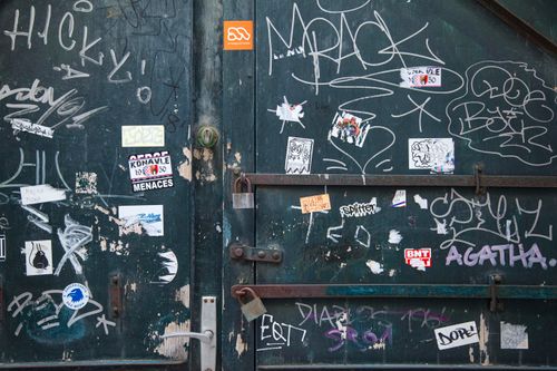 Free Weathered metal door with locks and doorhandle near white painted graffiti and small stickers in daylight Stock Photo