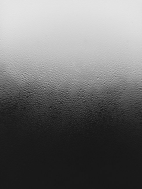 Black and white abstract texture of raindrops on a glass surface, captured vertically.