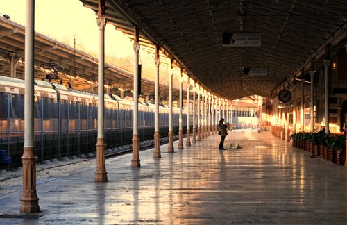 Free Long empty train station platform with a person and their dog at sunset, creating a serene golden atmosphere. Stock Photo