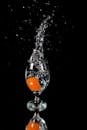 一颗橙色水果溅入黑暗背景下的一杯透明水中