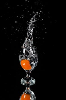 一颗橙色水果溅入黑暗背景下的一杯透明水中