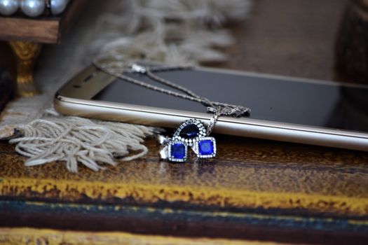 Close-up of a sparkling necklace with blue gemstones resting on a smartphone, placed on a rustic table.