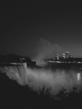 Black and white night scene of Niagara Falls with city lights in the background.