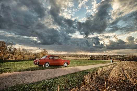 A vintage red car parked on a rural path under dramatic skies, perfect for travel themes.