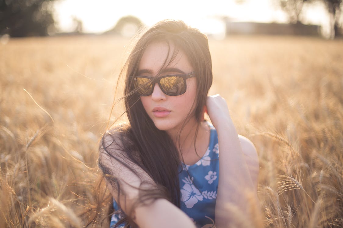 Free Woman Wearing Blue and White Floral Sleeveless Dress Sitting on Grass Stock Photo