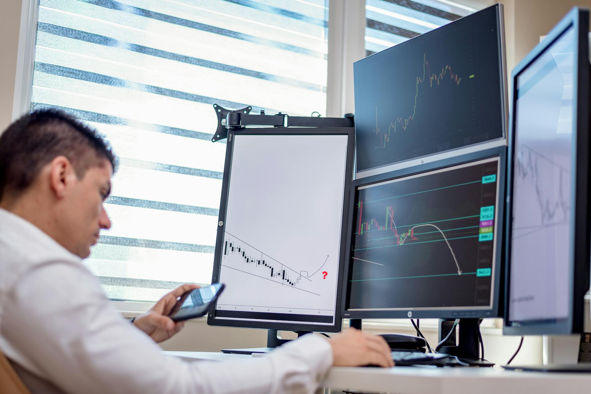 A stock trader analyzes financial data on multiple computer screens in an office setting.