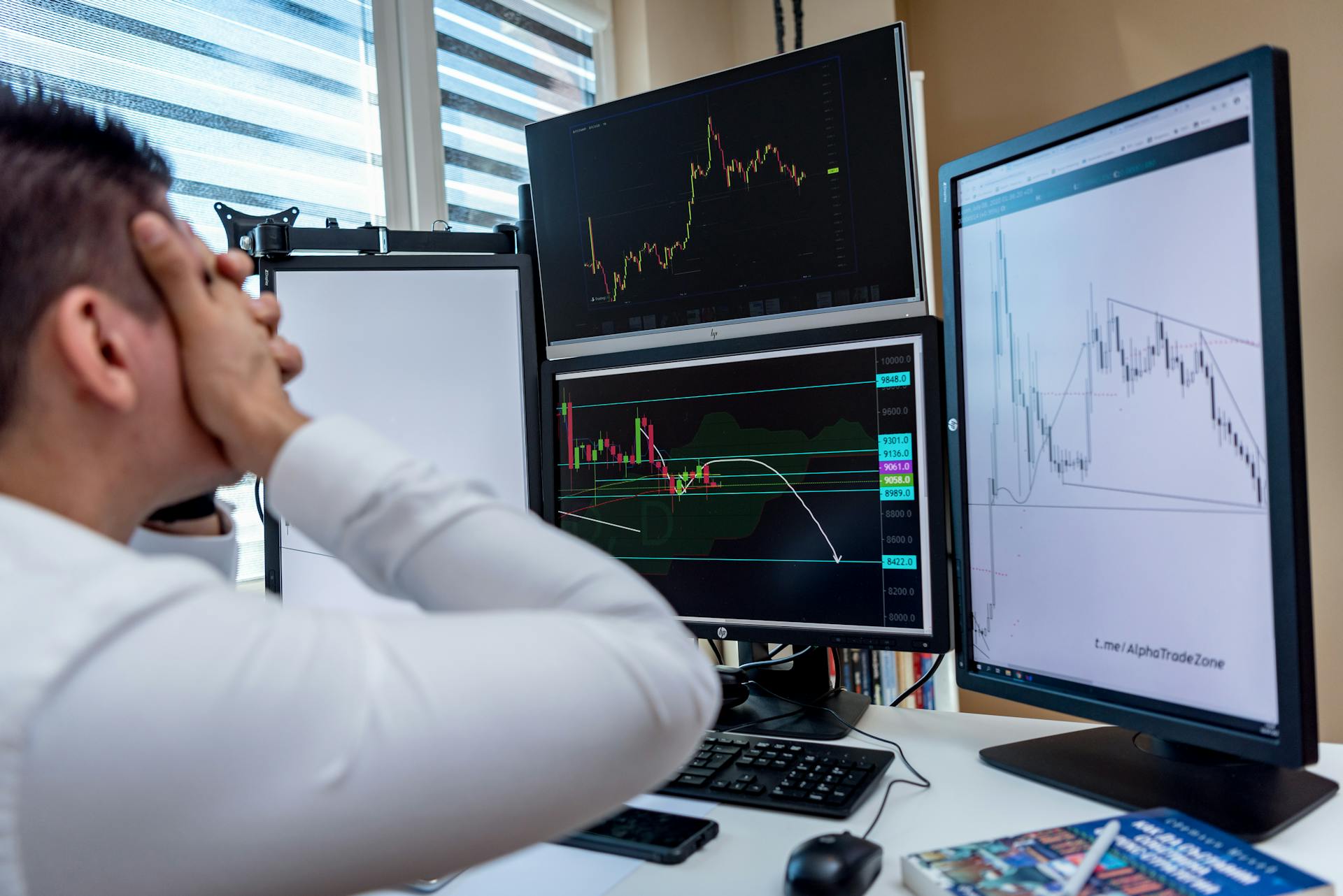 Frustrated man monitoring multiple trading graphs on computer screens in an office setting.