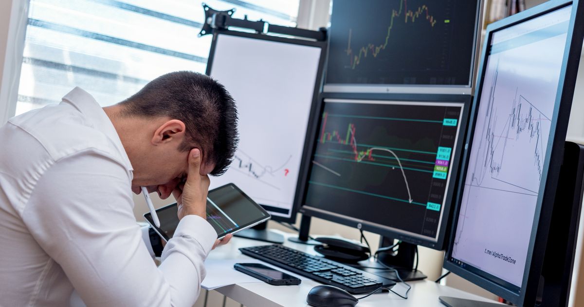 Trader with head in hand in front of multiple monitors showing charts