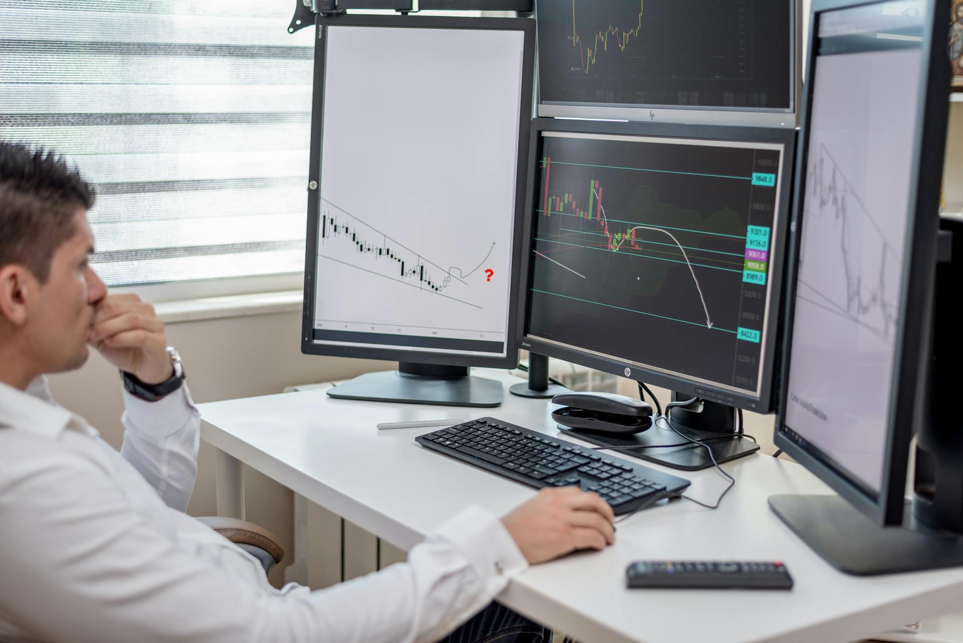 Business professional analyzing financial data on multiple computer monitors at his workspace.