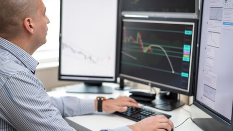 Businessman reviewing financial charts on multiple monitors in an office setting.