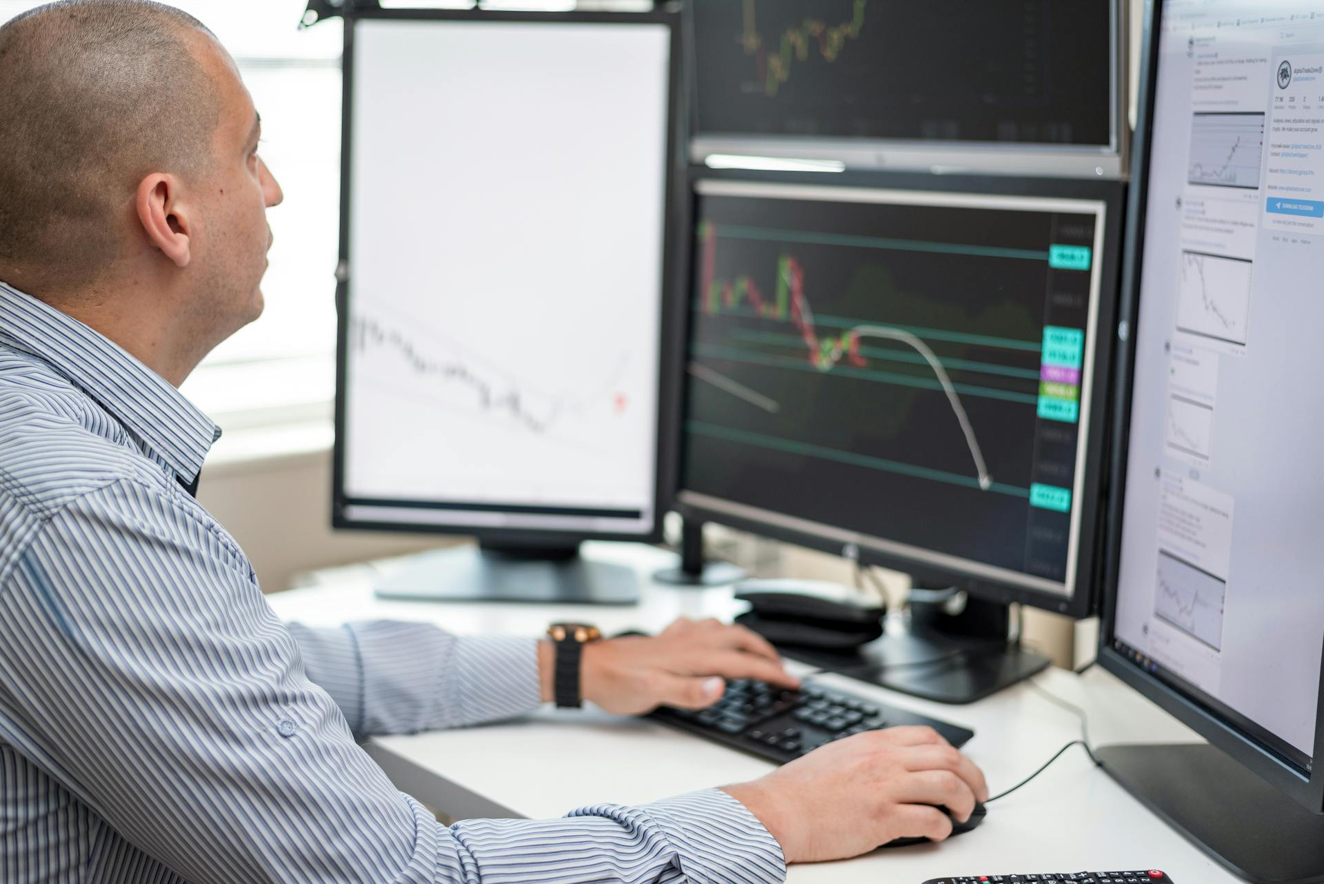 Businessman reviewing financial charts on multiple monitors in an office setting.