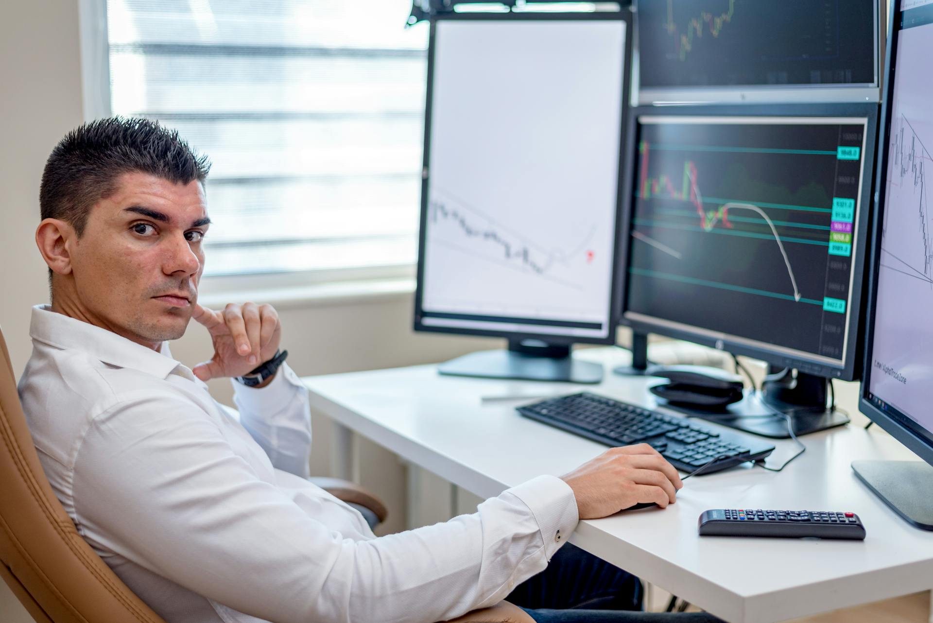 Professional stock market analyst monitoring data on multiple screens at a workstation.