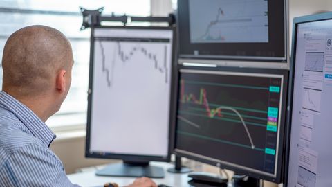 Trader analyzing financial data on multiple monitors in an office setting.
