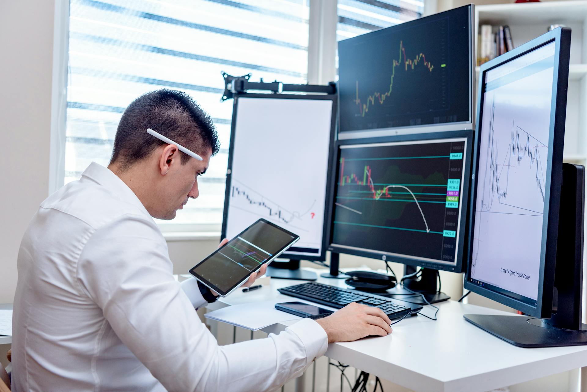 Professional analyzing stock market graphs on multiple monitors at work desk.