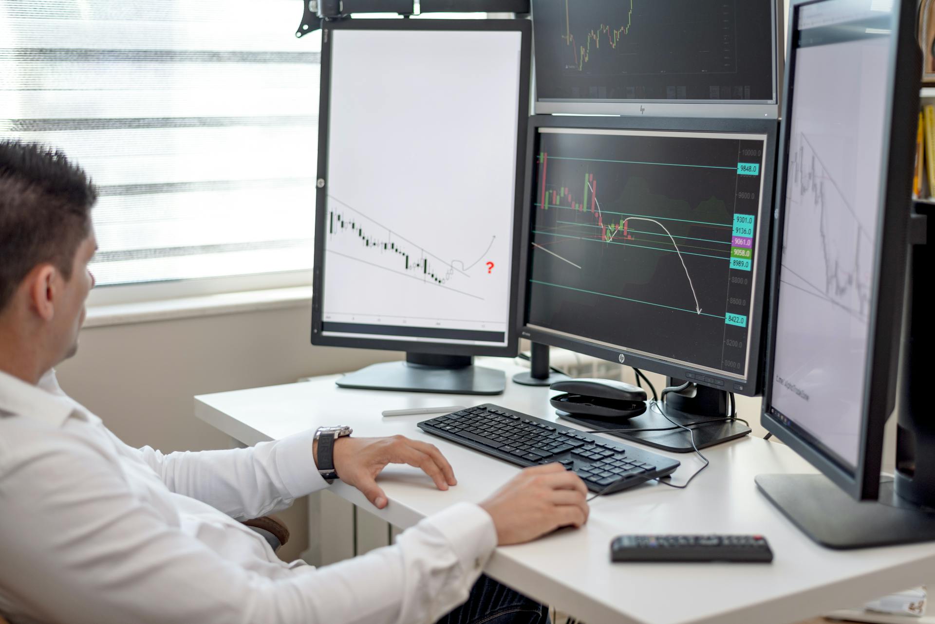 A businessman at his desk analyzing financial charts on multiple monitors.