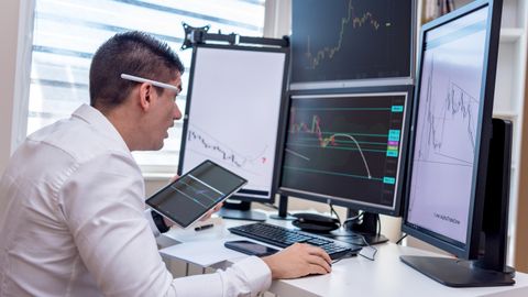 A man analyzing stock market graphs on multiple screens at a workstation.