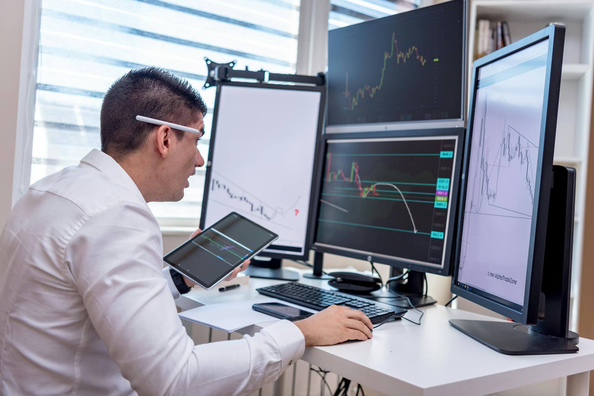 A man analyzing stock market graphs on multiple screens at a workstation.