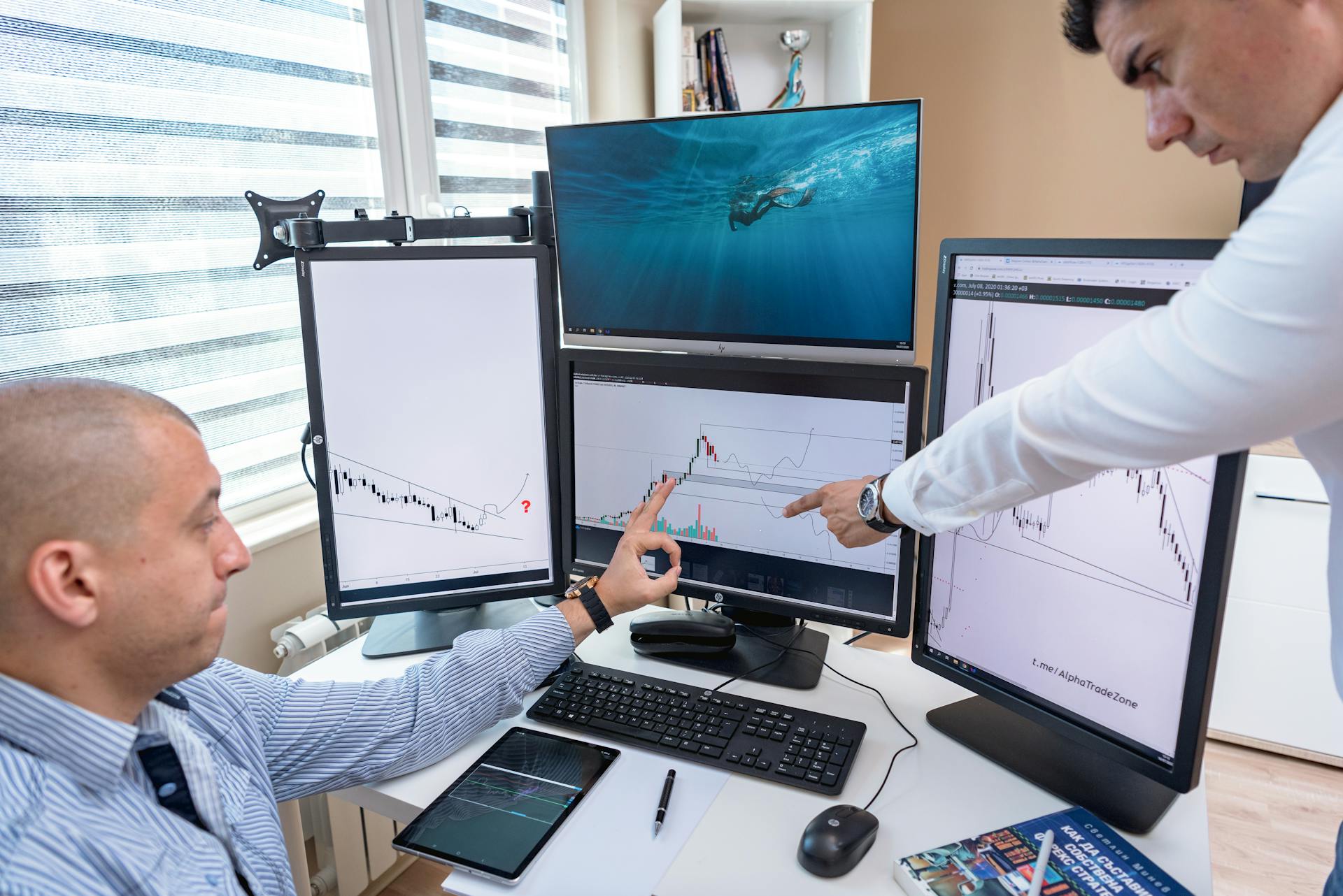 Two business professionals analyzing financial data on multiple computer screens in an office setting.