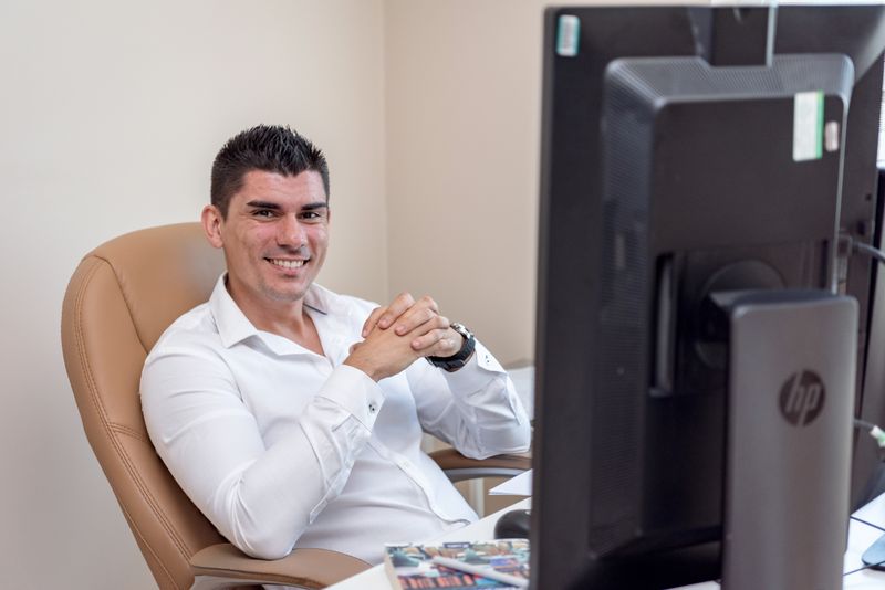 Confident man sitting at desk in office, smiling at computer screen