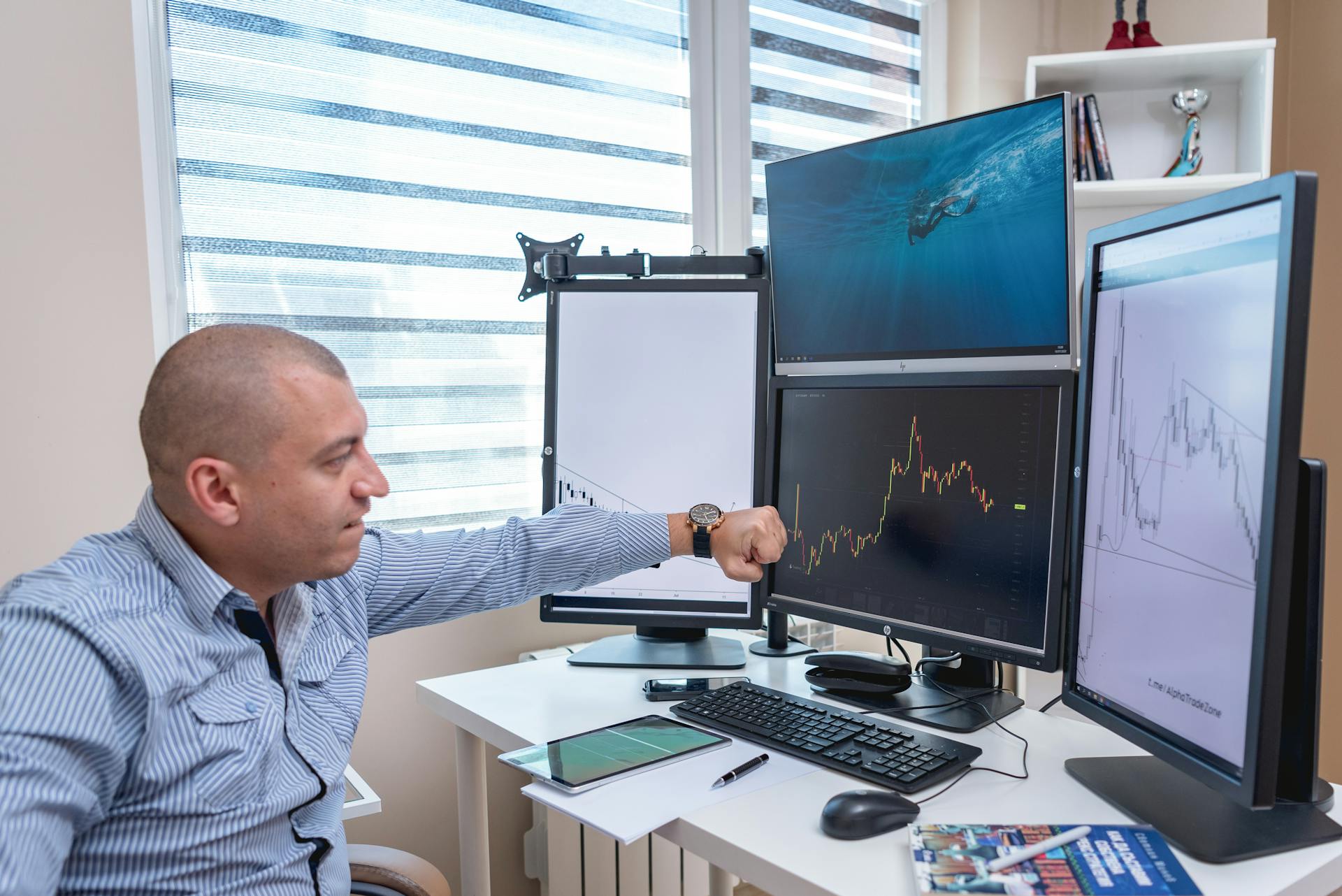 A trader analyzing market trends on multiple monitors at an indoor office desk.