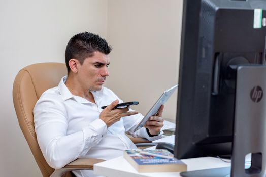 Focused businessman working with smartphone and tablet in a modern office.