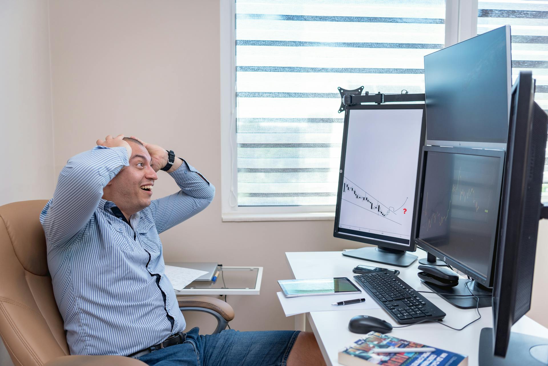 A thrilled man reacts to financial market trends on multiple monitors in a modern office setup.