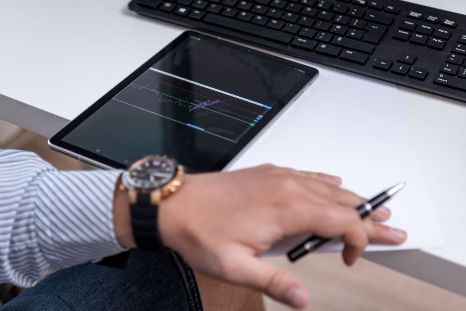 Close-up of a business worker analyzing charts on a tablet with a pen on a desk.