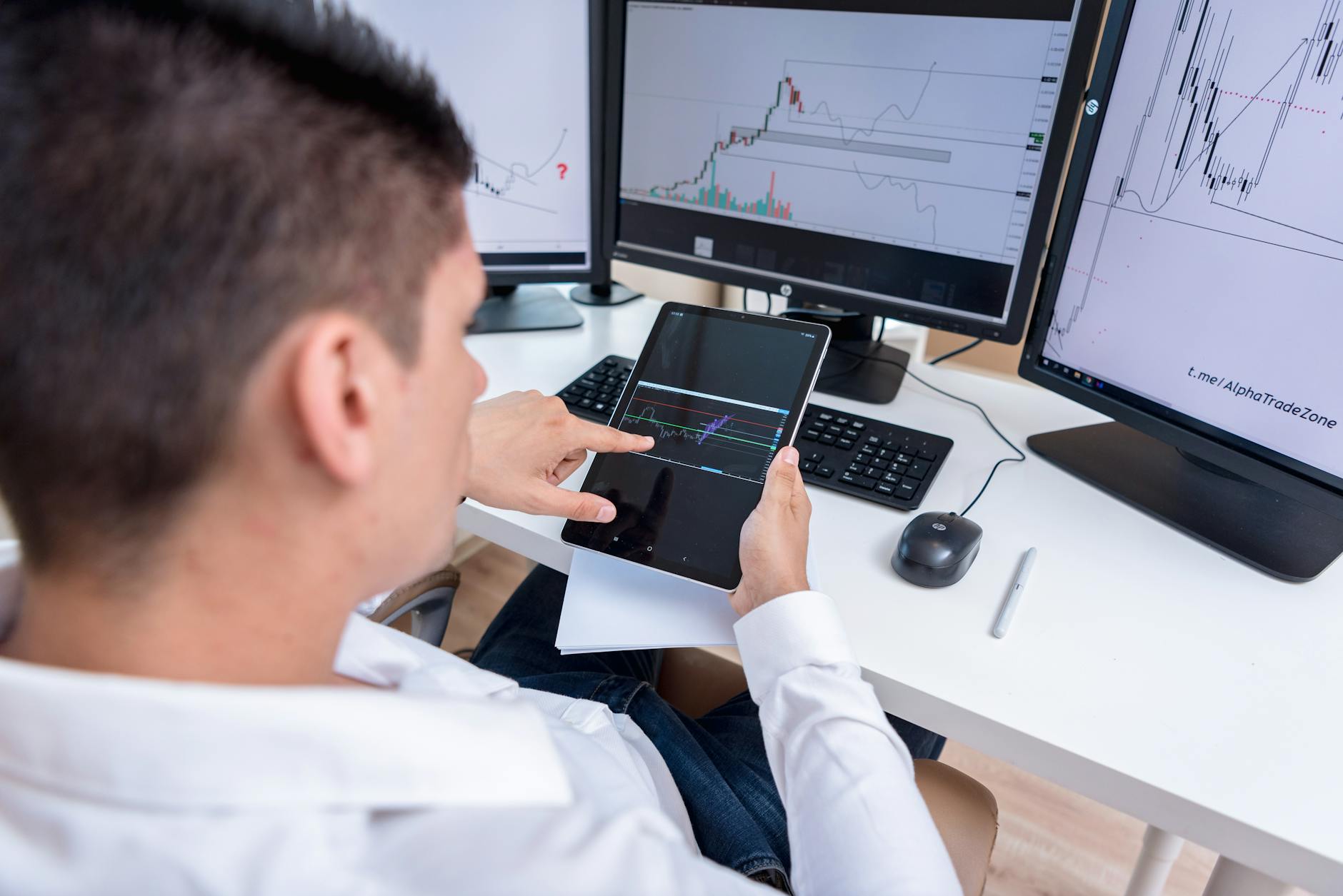 A stock trader analyzing cryptocurrency charts on multiple monitors and a tablet.