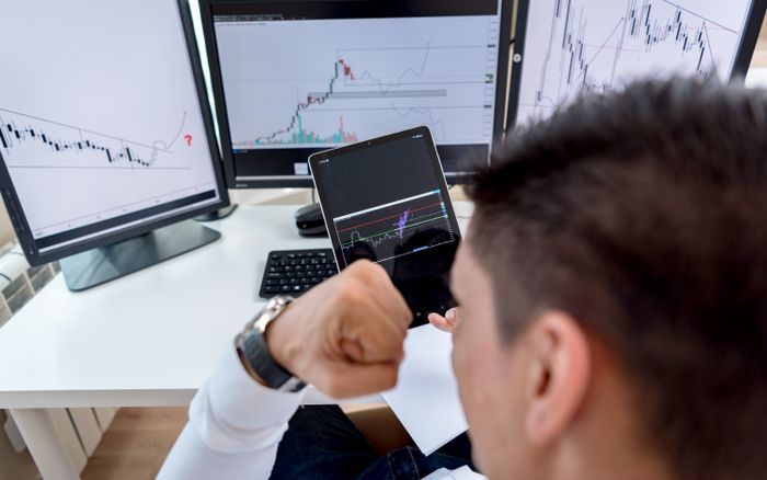 A trader confidently viewing stock market charts on multiple monitors in a modern workspace.