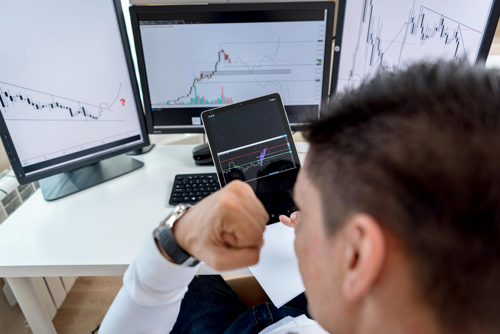 A trader confidently viewing stock market charts on multiple monitors in a modern workspace.