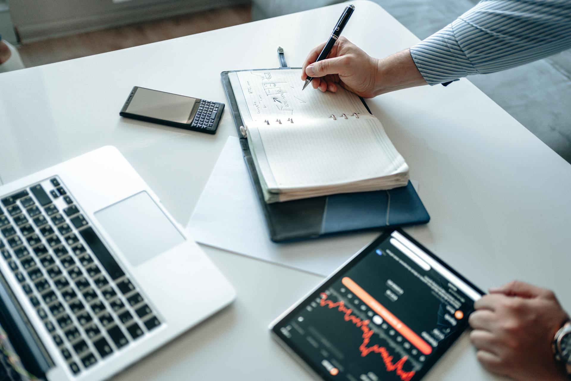 Person analyzing financial data on laptop, tablet, and notebook.